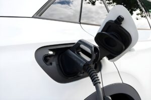 Close-up of a black electric vehicle charging cable plugged into the side port of a white car.
