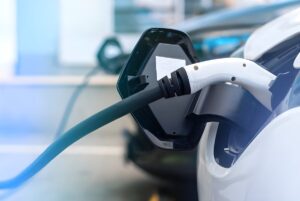 Close-up of a white electric vehicle charging with a black and white plug at a public charging station.