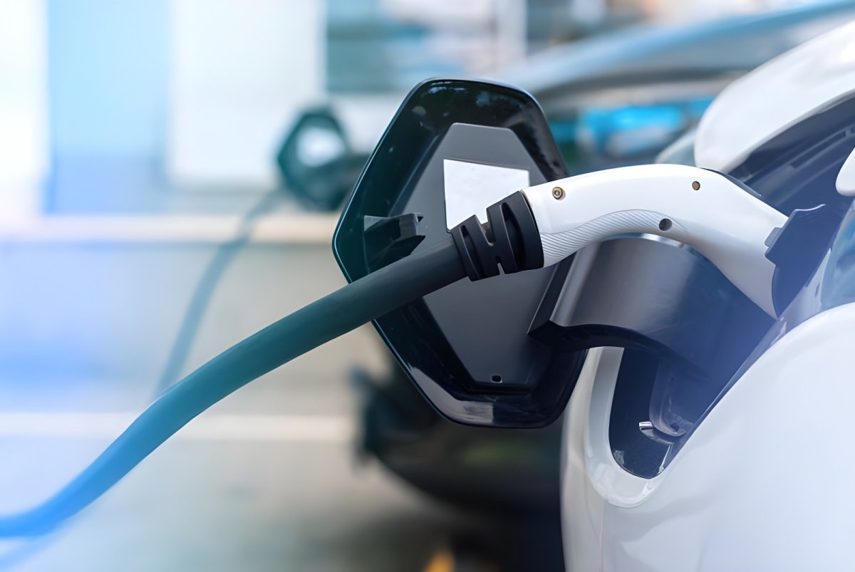 Close-up of a white electric vehicle charging with a black and white plug at a public charging station.