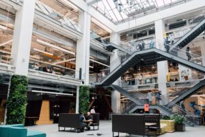 Multi-story modern office atrium with industrial steel staircases, glass ceilings, and vertical green plant walls.