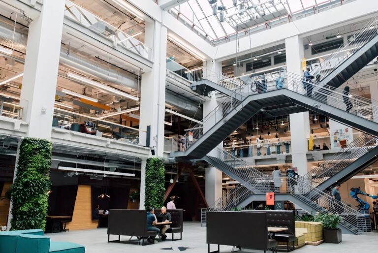 Multi-story modern office atrium with industrial steel staircases, glass ceilings, and vertical green plant walls.