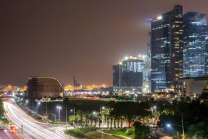 Long exposure night view of illuminated Singapore skyscrapers and street lights overlooking a highway with vehicle light trails.