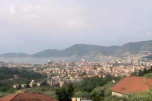 Elevated wide-angle view of La Spezia, Italy, featuring the coastal city, harbor, and surrounding green hills.