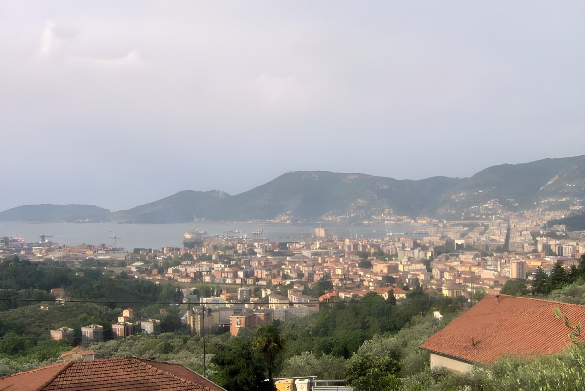 Elevated wide-angle view of La Spezia, Italy, featuring the coastal city, harbor, and surrounding green hills.