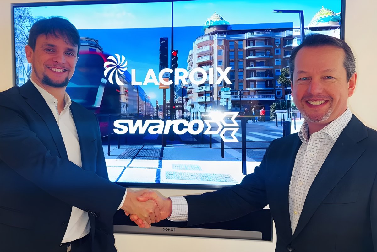 Two men in suits shake hands in front of a screen displaying the LACROIX and SWARCO logos over a city street scene.