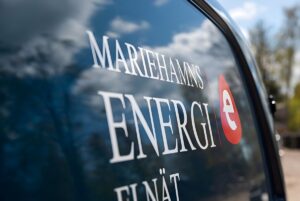 Close-up of a Mariehamns Energi logo on a blue vehicle window reflecting clouds and trees.