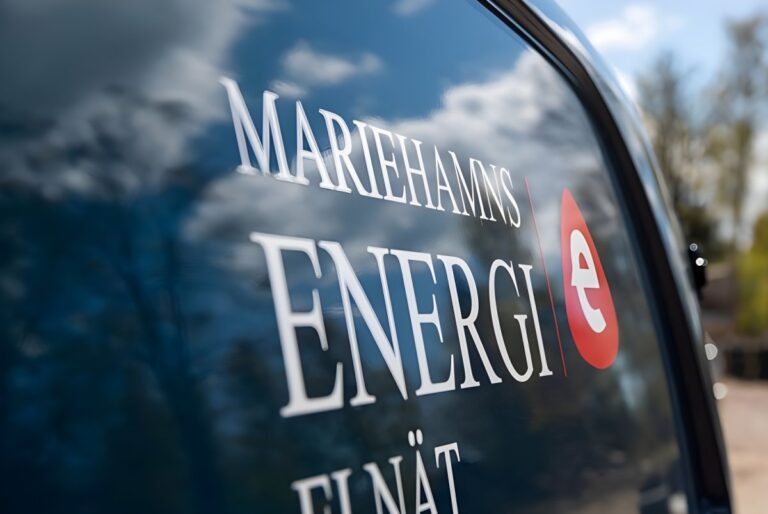 Close-up of a Mariehamns Energi logo on a blue vehicle window reflecting clouds and trees.