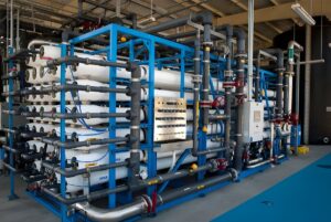 Industrial reverse osmosis desalination system with white membrane pressure vessels and blue steel framing.