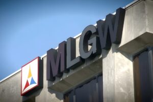 Low-angle view of the MLGW logo and signage on the exterior of a concrete utility building under a clear blue sky.