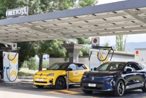 Renault electric vehicles charging at a Free To X station under a solar panel canopy at an Autostrade per l'Italia site.