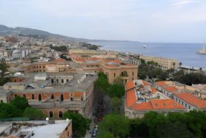 High-angle view of the San Filippo del Mela cityscape featuring terracotta rooftops and a coastal harbor in Sicily.