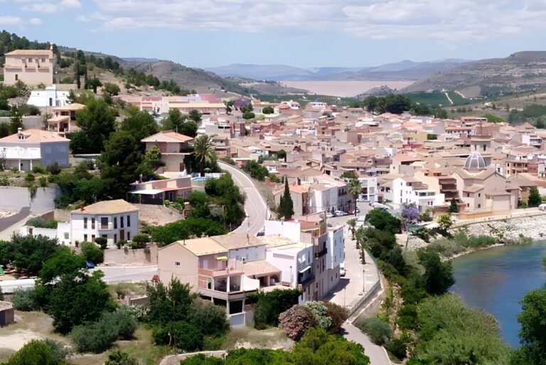 Aerial view of Sumacàrcer, Spain, featuring residential buildings, a winding road, and the Júcar River.