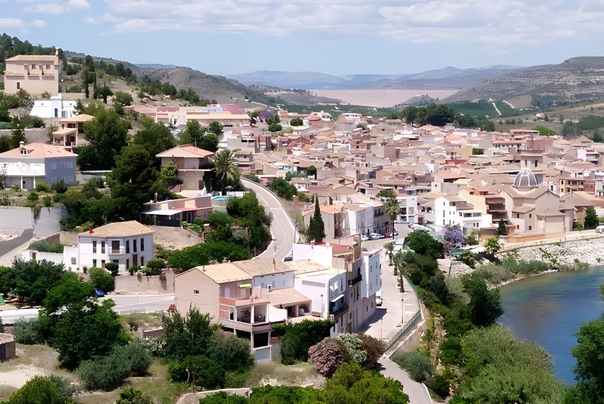 Aerial view of Sumacàrcer, Spain, featuring residential buildings, a winding road, and the Júcar River.