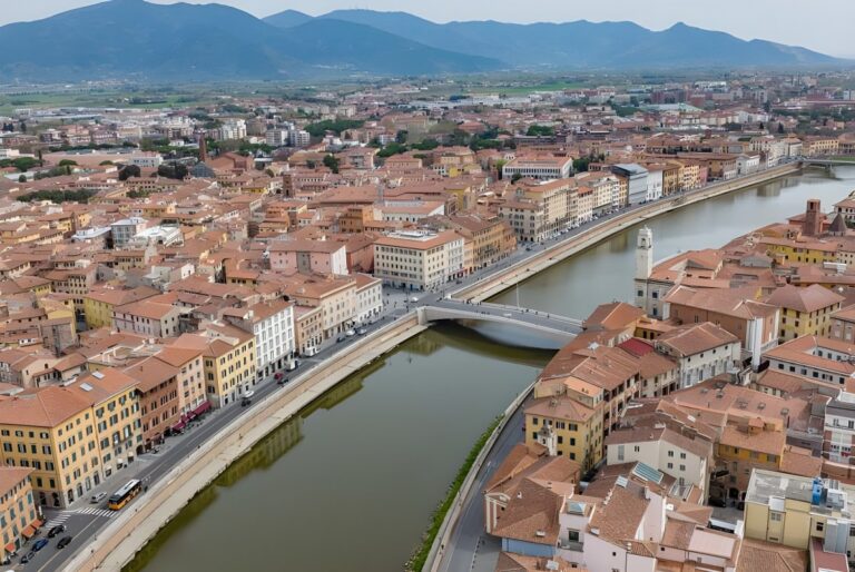 Aerial view of the Arno River flowing through Pisa, Italy, featuring the Ponte di Mezzo and historic terracotta buildings.