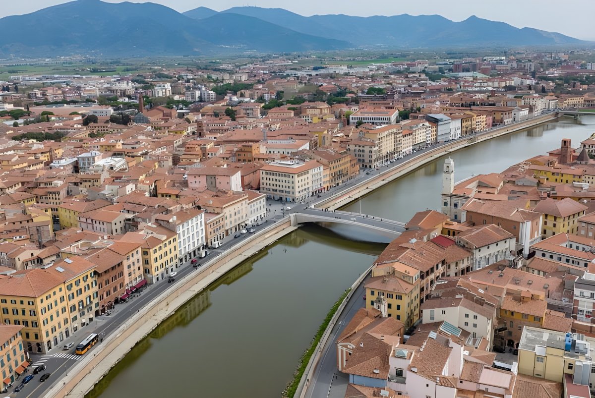 Aerial view of the Arno River flowing through Pisa, Italy, featuring the Ponte di Mezzo and historic terracotta buildings.