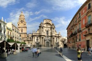 Pedestrians in the Plaza Cardenal Belluga facing the Murcia Cathedral and Episcopal Palace in Spain.