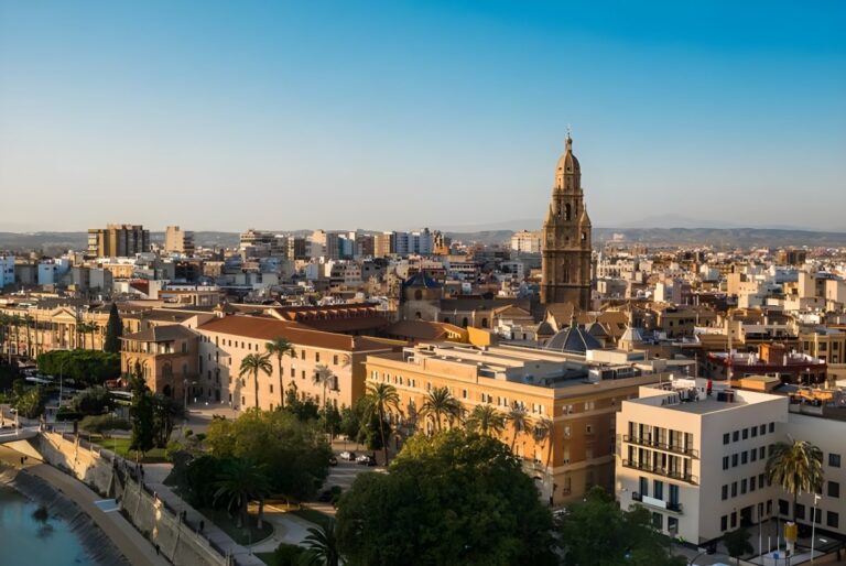 High-angle cityscape of Murcia, Spain, featuring the Murcia Cathedral bell tower and urban buildings under a clear sky.