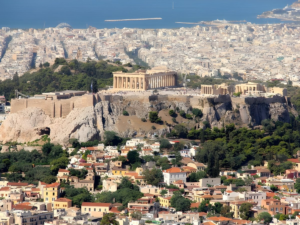 Aerial view of the Parthenon and Acropolis of Athens overlooking a dense urban landscape and the Saronic Gulf.