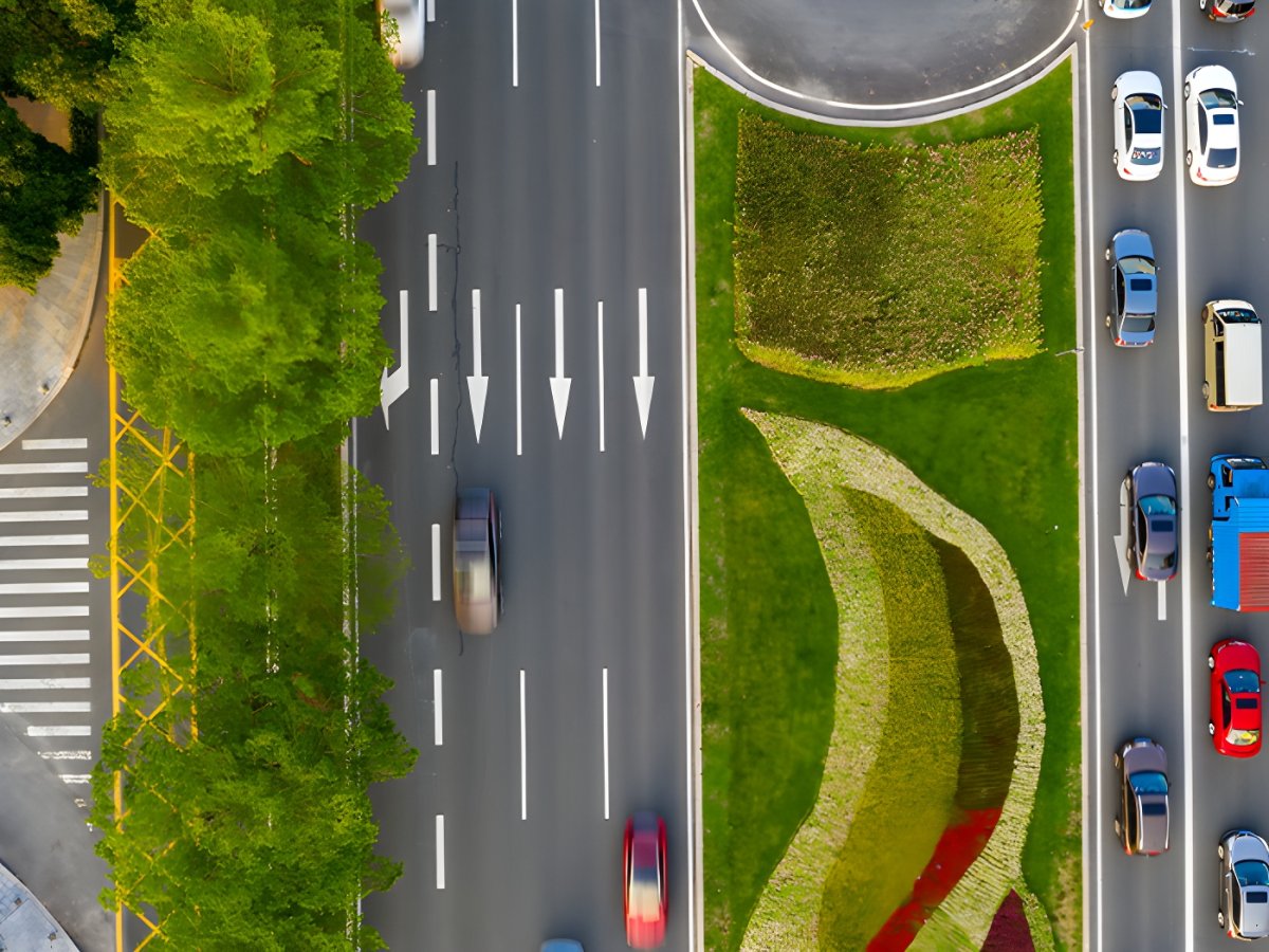 Top-down aerial view of cars driving on a multi-lane urban highway with painted directional arrows and a landscaped median.