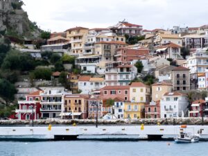 Colorful multi-story buildings and houses built into a hillside overlooking a harbor and concrete pier in Parga, Greece.