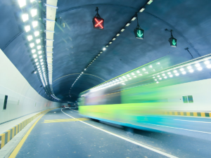 Motion blur of a green bus driving through a brightly lit highway tunnel with overhead digital lane control signals.