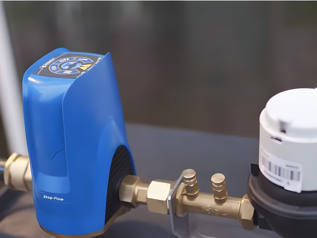 A blue Hydrelis Stop-Flow water leak detection device installed on a brass pipe next to a white water meter.