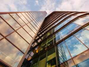 Low-angle view of a modern glass skyscraper reflecting a blue sky with white clouds.