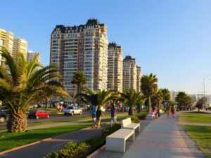 High-rise apartment buildings along a palm tree-lined coastal boulevard with pedestrians and traffic in Viña del Mar.
