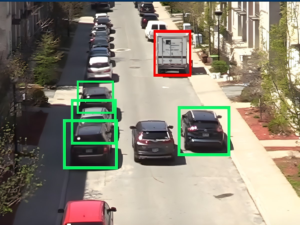 Overhead view of city street traffic with green and red digital bounding boxes identifying parked and moving vehicles.