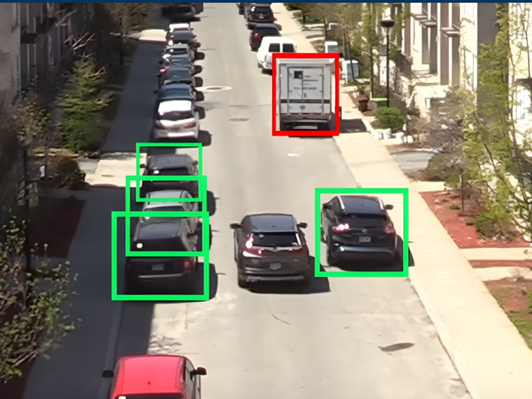 Overhead view of city street traffic with green and red digital bounding boxes identifying parked and moving vehicles.