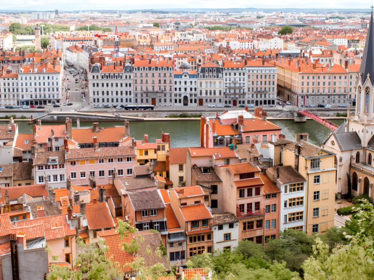 High-angle view of Lyon, France, featuring orange-roofed buildings along the Saône river and the Passerelle Saint-Georges.