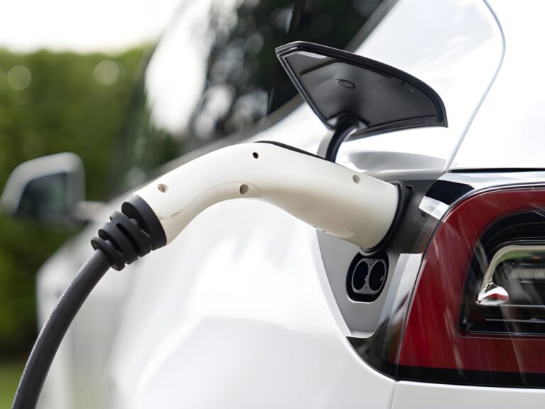 Close-up of a white electric vehicle charging with a white plug inserted into the rear side port.