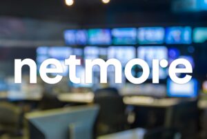Netmore logo overlaid on a blurred network operations center with multiple monitor screens and workstations.