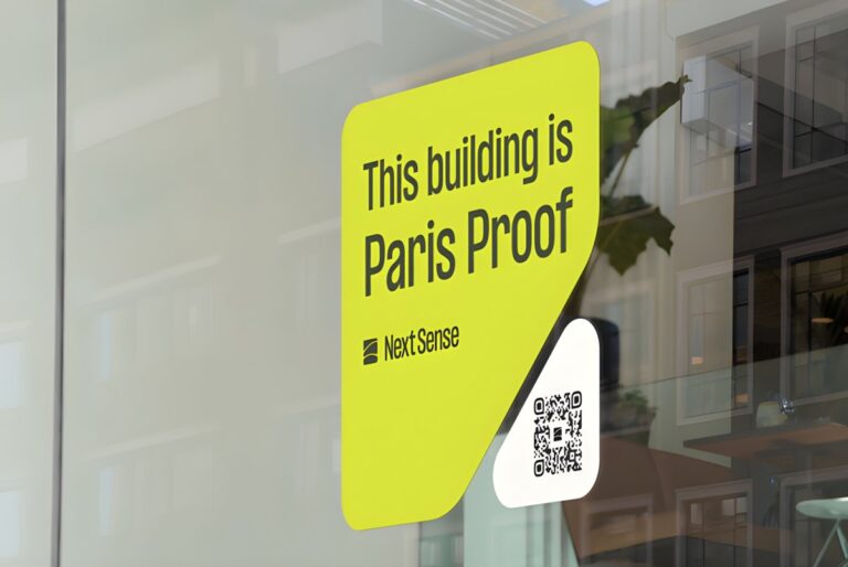 A Next Sense "Paris Proof" decal with a QR code on a glass window reflecting an office interior.