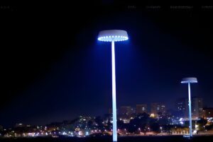 Two Omniflow smart poles with circular LED light fixtures illuminate a city skyline at night.