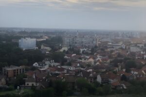 High-angle wide shot of the Oradea city skyline featuring red-tiled roofs and residential buildings under a cloudy sky.