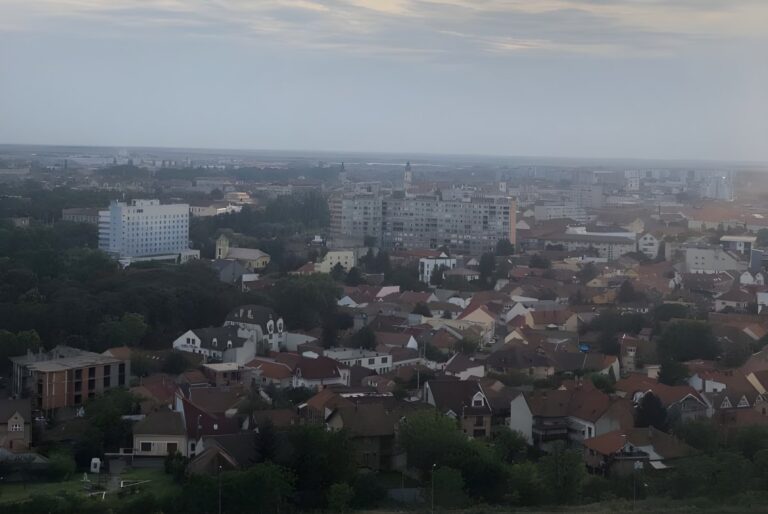 High-angle wide shot of the Oradea city skyline featuring red-tiled roofs and residential buildings under a cloudy sky.