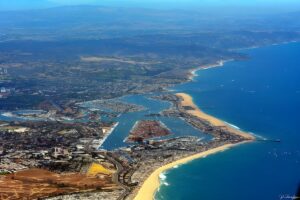 Aerial view of Newport Harbor and the Orange County coastline with sandy beaches, urban development, and distant mountains.
