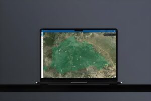 Laptop displaying the OroraTech wildfire intelligence platform with a green satellite map overlay on a dark background.