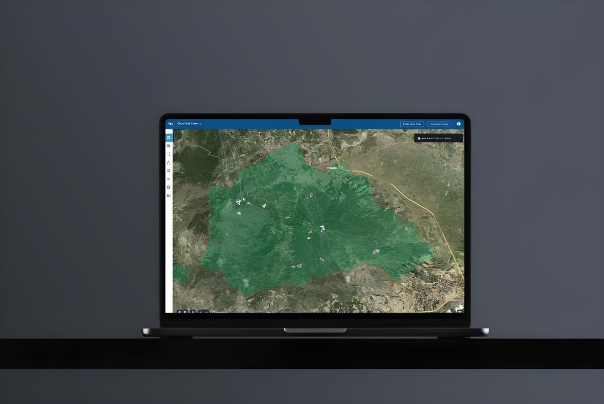 Laptop displaying the OroraTech wildfire intelligence platform with a green satellite map overlay on a dark background.