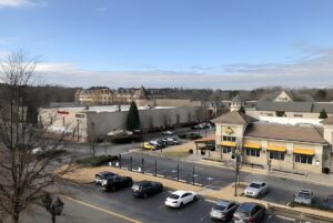 Elevated view of a suburban shopping center in Peachtree Corners with parked cars, retail buildings, and a clear sky.