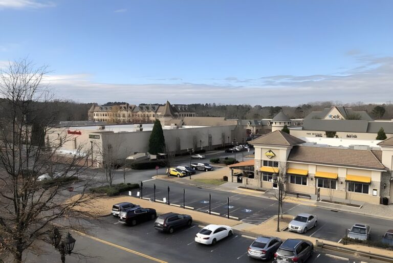 Elevated view of a suburban shopping center in Peachtree Corners with parked cars, retail buildings, and a clear sky.