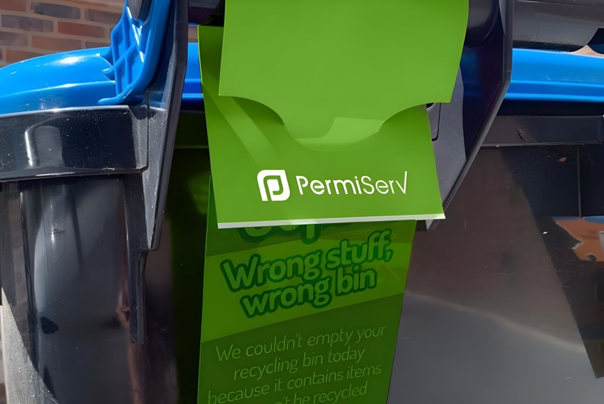 A green PermiServ tag hanging from the handle of a blue and black recycling bin.
