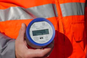 A technician in high-visibility orange clothing holds a Kamstrup flowIQ 2200 ultrasonic smart water meter.