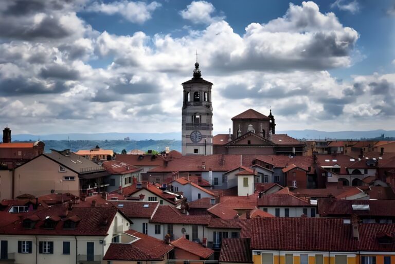 Skyline of a Piedmont town featuring red-tiled rooftops and a central stone clock tower under a cloudy sky.