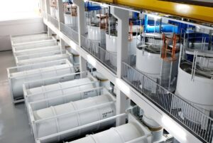 Industrial facility with rows of large white Envac waste collection tanks and pneumatic piping systems.