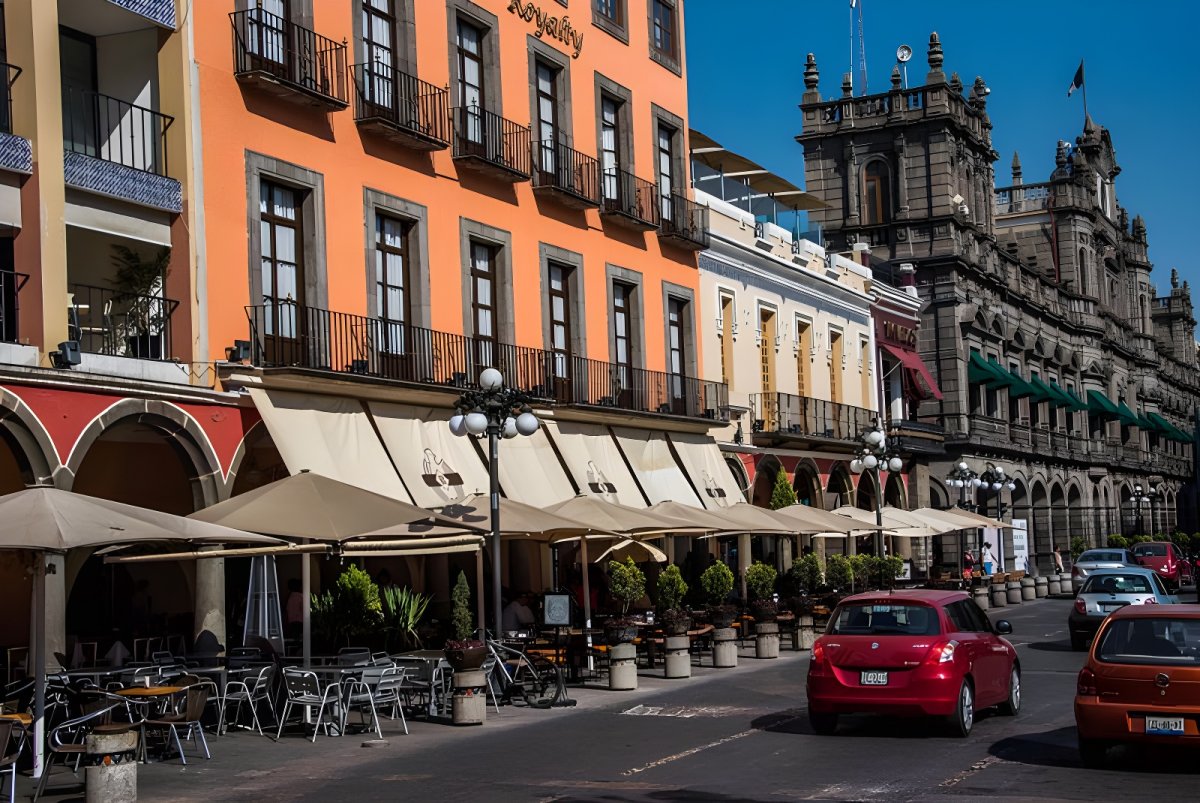 Street-level view of historic buildings, sidewalk cafes with umbrellas, and traffic in downtown Puebla, Mexico.
