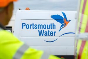 Portsmouth Water logo and kingfisher graphic on the side of a white utility van behind a worker in high-visibility gear.