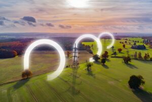 Aerial view of a high-voltage transmission tower in a rural field with glowing digital rings encircling the power lines.