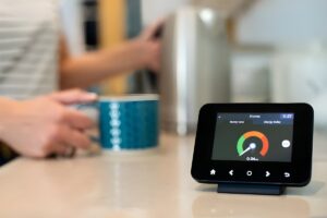 A smart meter in-home display showing energy usage on a kitchen counter next to a person holding a mug.